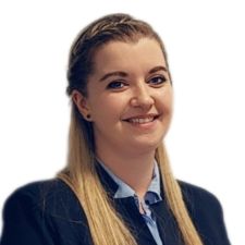 Na zdjęciu widać kobietę z długimi blond włosami, ubraną w ciemną marynarkę i niebieską koszulę.